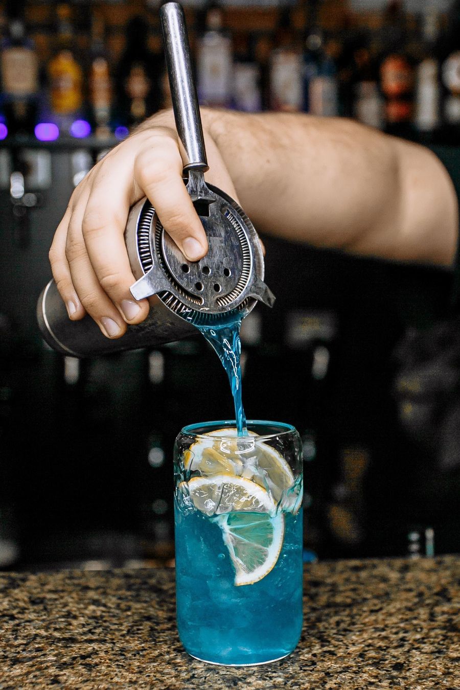 Bright blue mocktail strained over ice and lemon wheels